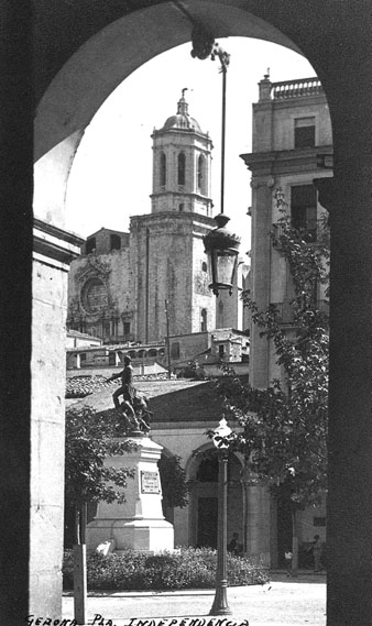 Vista parcial de la plaça de la Independència des d'un dels arcs de la zona porxada. En primer terme, el monument als Defensors de Girona el 1808 i 1809. Al fons, la Catedral de Girona. 1939-1940