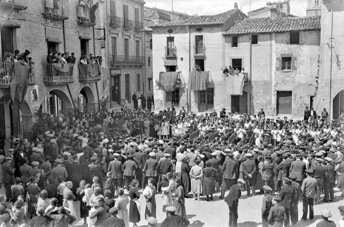 Celebració de la festa d'Homenatge a la Vellesa a Amer. Ancians i assistents asseguts en bancs enmig de la plaça del poble escoltant els parlaments de les autoritats. 1935