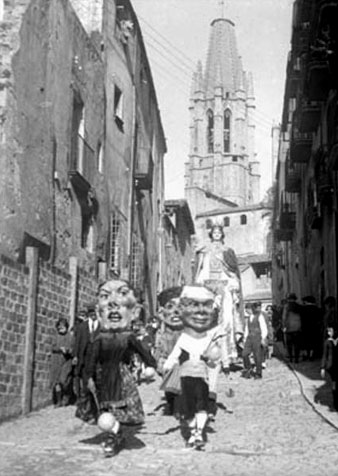 Capgrossos, gegants i nens a la pujada de Sant Feliu, amb el campanar de l'esgl&eacute;sia al fons
