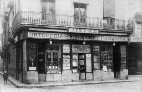Establiment Ortopèdia-farmàcia Doctor Roca a la plaça de l'Oli. Façana de l'establiment on apareix el rètol de la farmàcia i el de l'administració de loteria nº 2. 1935-1940