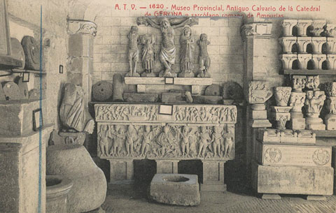 Galeria del claustre del monestir de Sant Pere de Galligants habilitada com a sala del Museu Arqueològic Provincial a Girona. S'observa l'antic calvari de la Catedral de Girona i un sarcòfag romà d'Empúries. 1910-1920