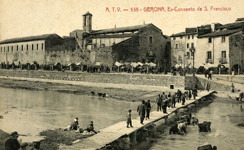 El convent de Sant Francesc de Paula, conegut com els Mínims, i la palanca de l'Areny vistos de l'altre costat del riu. Paral·lel al riu, el passeig General Mendoza ple de carruatges durant un dia de mercat i a la dreta, la rambla Pi i Margall. S'observen bugaderes rentant roba al riu. 1905