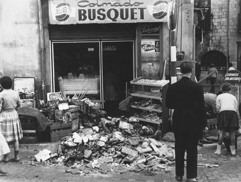 Gent traient material afectat per les inundacions a l'exterior del Colmado Busquet, a la plaa Catalunya. A la dreta, el carrer Albereda. 1962
