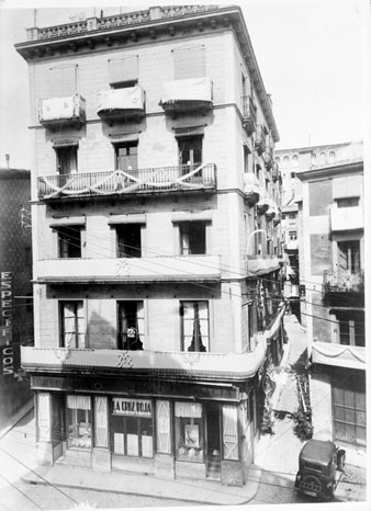 Façana d'un bloc de pisos, situat a la plaça de l'Oli. A la planta baixa hi ha la fàrmcia Roca