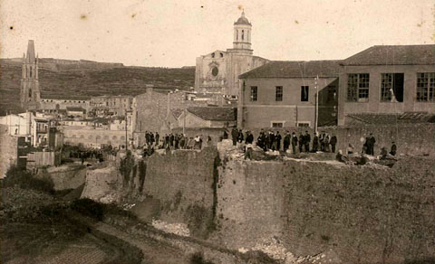 Enderrocament de la muralla del Mercadal a la zona de la Gran Via, a l'altura del baluard de la Santa Creu. En primer terme a la dreta, les naus de la fàbrica Gròber. Al fons d'esquerra a dreta, la muntanya de Montjuïc amb el castell, el campanar de l'església de Sant Feliu i la Catedral de Girona. 1901-1908