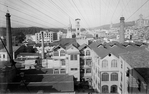 Vista parcial del barri del Mercadal. S'observa, en un primer pla, la f&agrave;brica Gr&ograve;ber, els magatzems i les xemeneies. Al fons, a la part central, el campanar neog&ograve;tic de l'esgl&eacute;sia de Santa Susanna i la Torre de les Aig&uuml;es