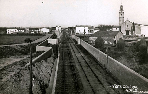 Vista de les vies de tren. Al fons s'observa la façana i el campanar de l'església de Sils. 1930-1936
