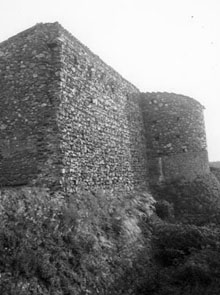 Restes de les muralles de Marzà amb una torre i al fons cases del poble. 1922-1931