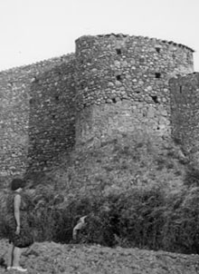 Restes de les muralles de Marzà amb una torre i una dona en primer terme. 1922-1931