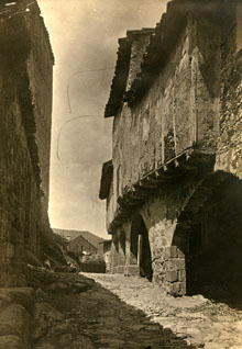 Carrer Vila Vella de Santa Pau. A l'esquerra, mur del castell de Santa Pau. A la dreta, porxo amb arcades d'uns habitatges. 1916